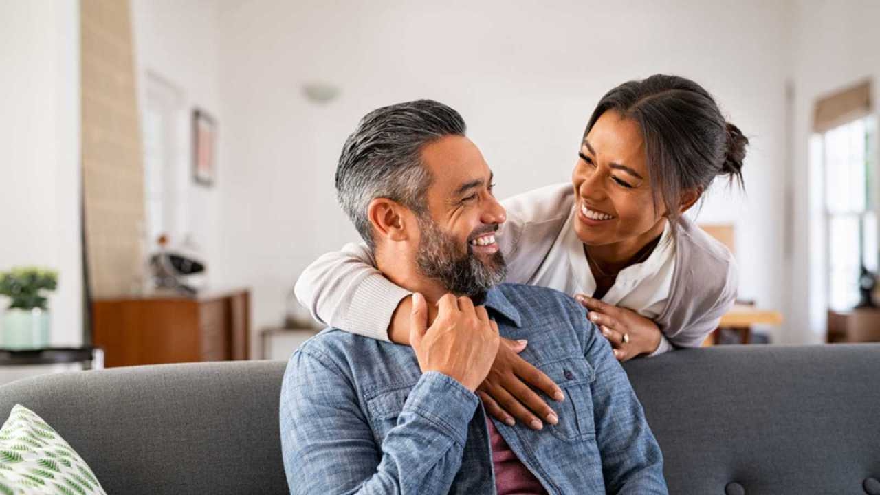 Happy Couple smiling at one another on a couch.