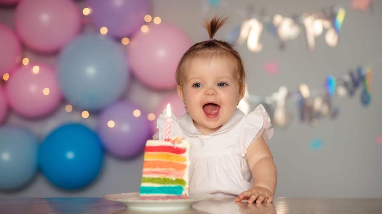 Happy one year old baby with rainbow birthday cake.