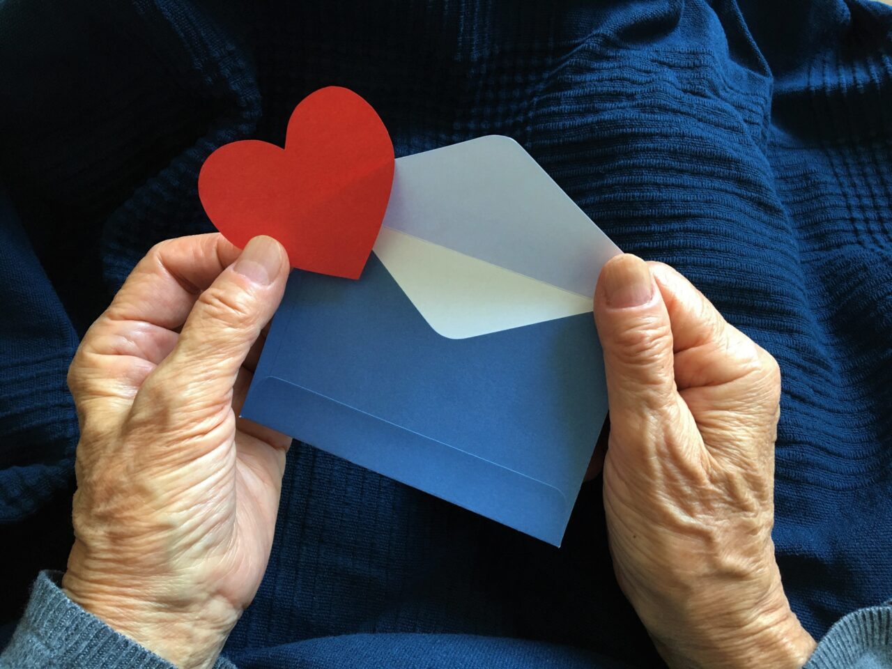 A blue envelope and a red heart in the hands of an elderly woman.