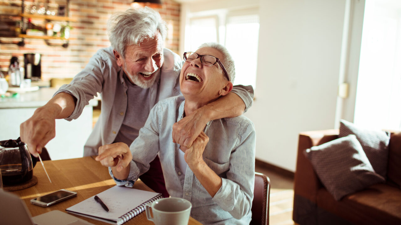 Happy senior couple laugh at computer.