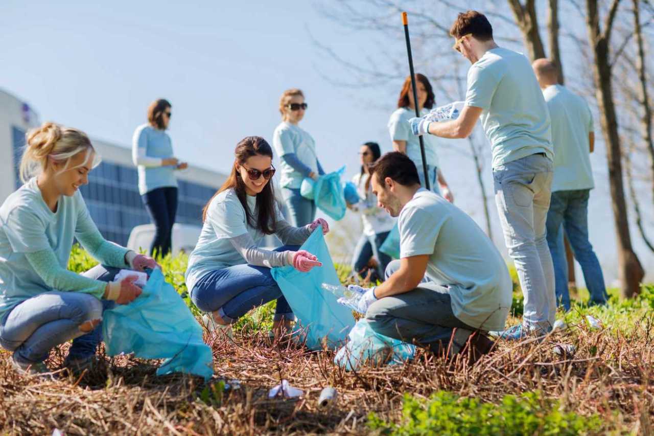 group of happy volunteers with garbage bags cleaning area in park.