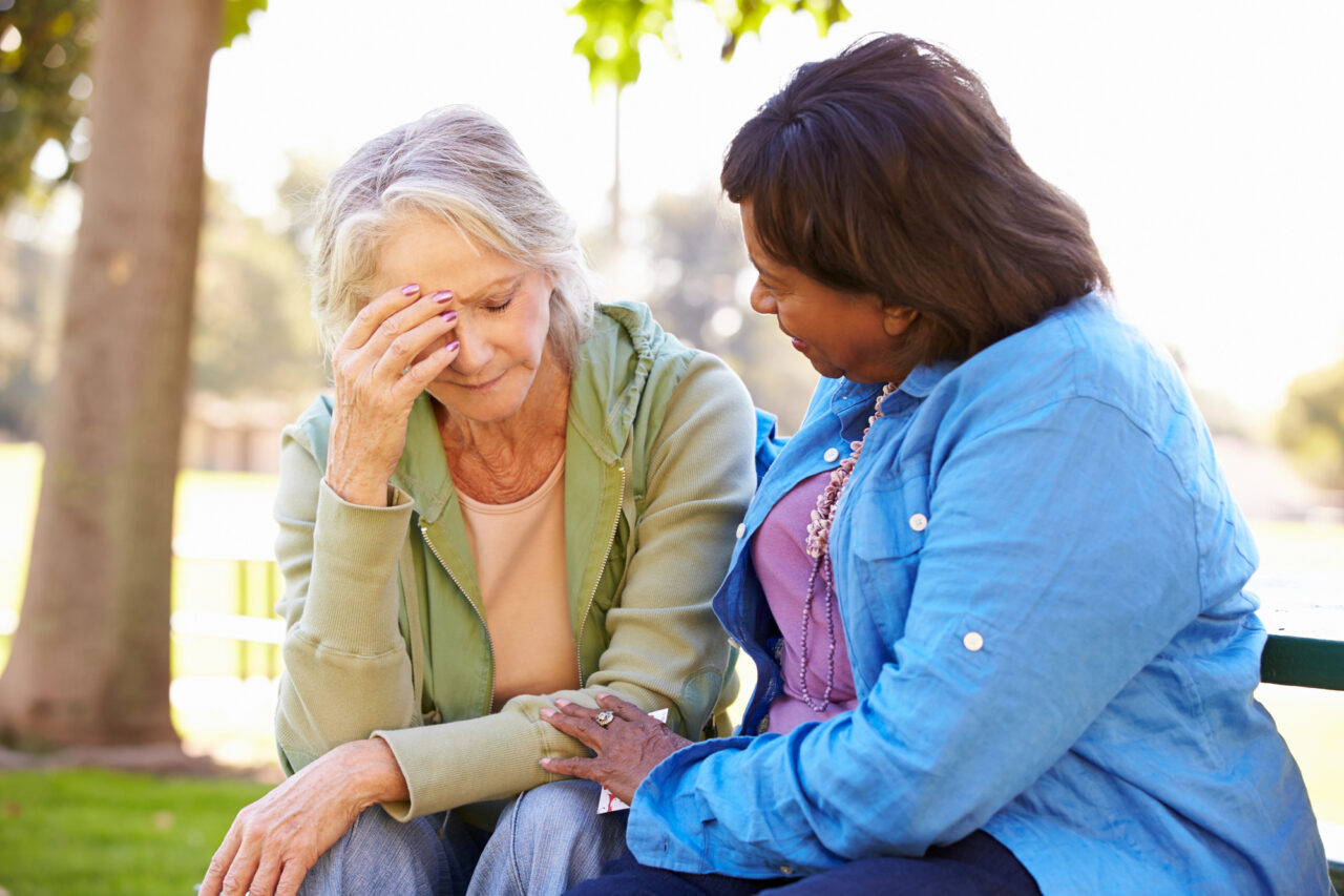 Woman Comforting Unhappy Senior Friend Outdoors.