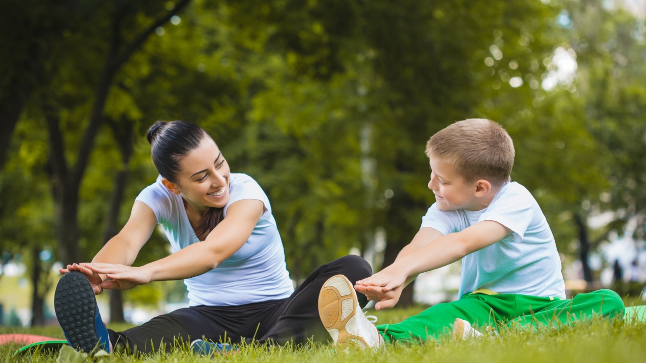 Mother and teen son stretch together on the lawn.